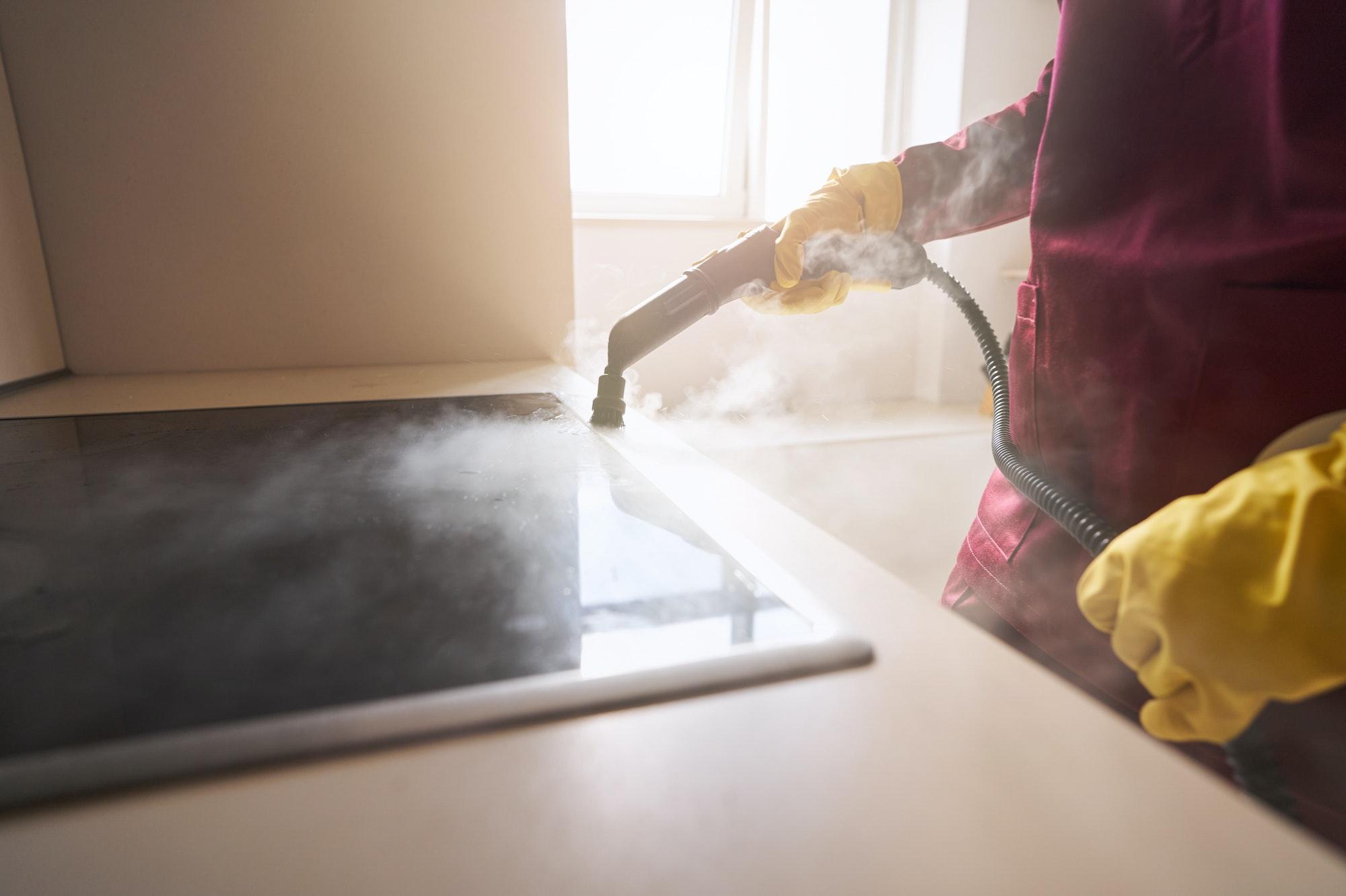 Cleaning person in rubber gloves steam-cleaning countertop