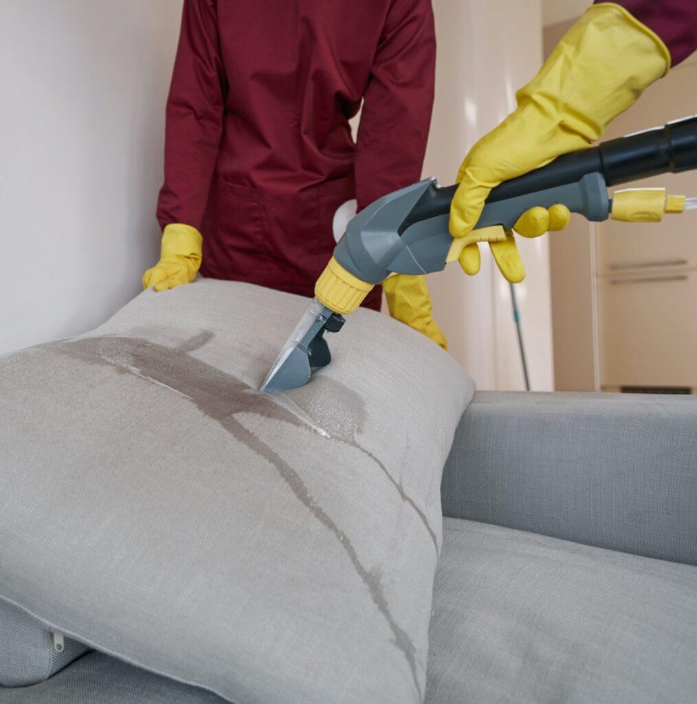 Two workers in rubber gloves steam-cleaning couch pillow